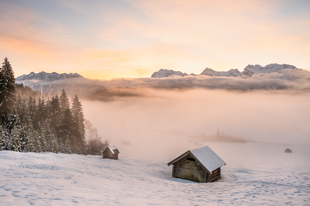 Zwei Holzhütten im Schnee mit dichtem Nebel im Hintergrund