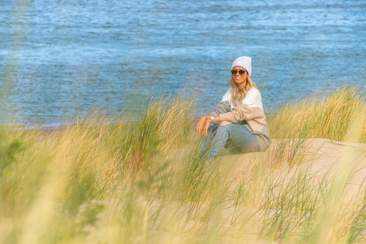 Frau sitzt in Dünen auf weißem Sandstrand an der Nordsee