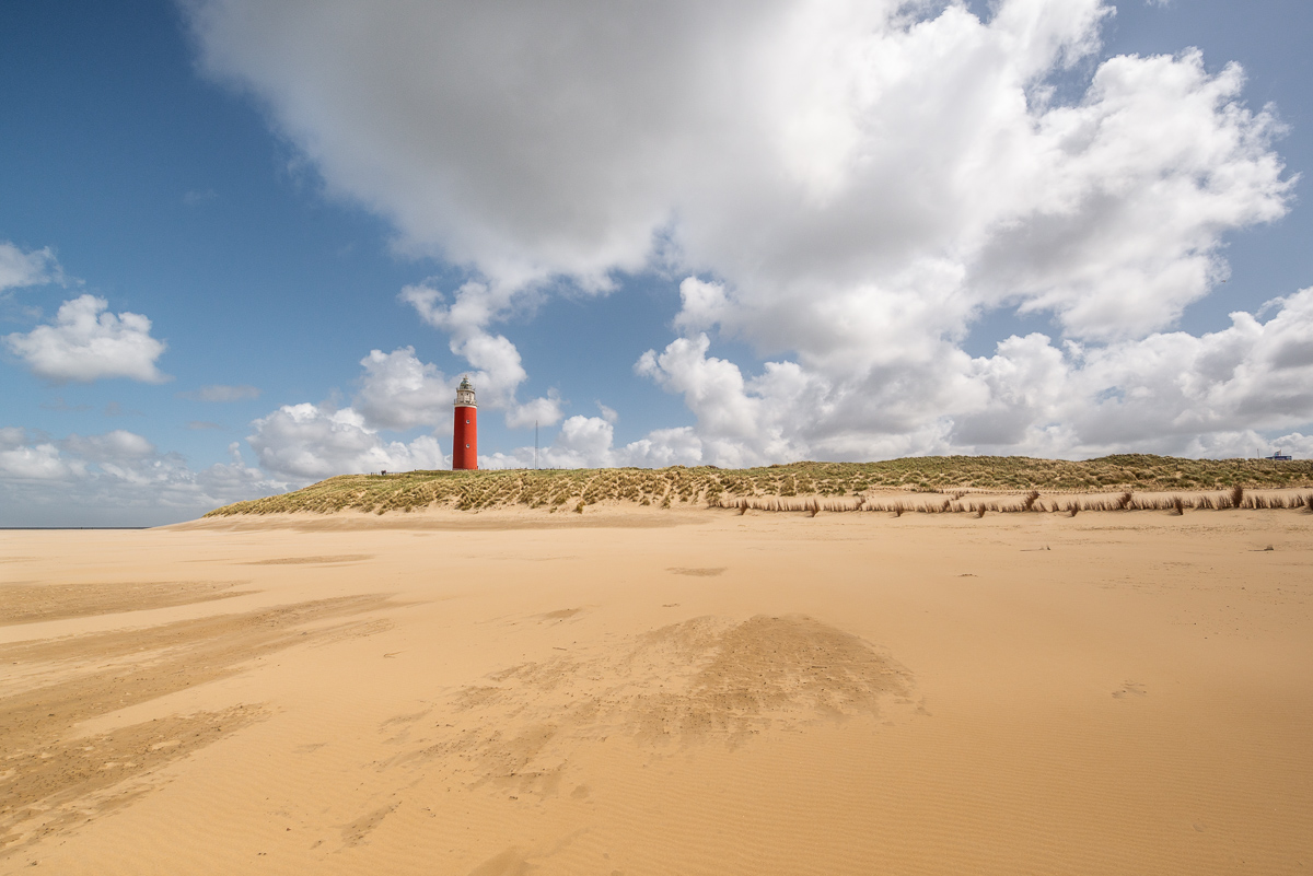 Weißer Sandstrand mit einem roten Leuchtturm im Hintergrund