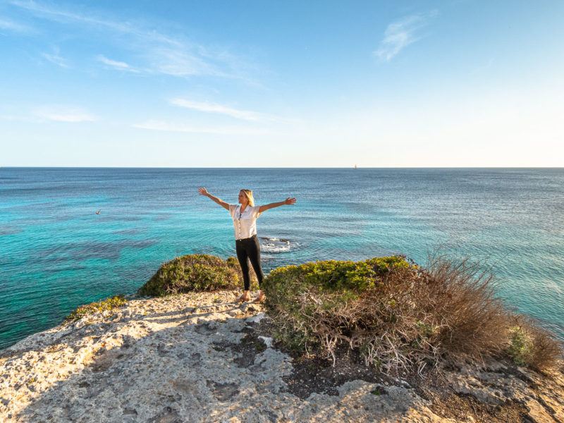Frau steht auf einem Felsen und blickt auf das Meer-Urlaubsblues