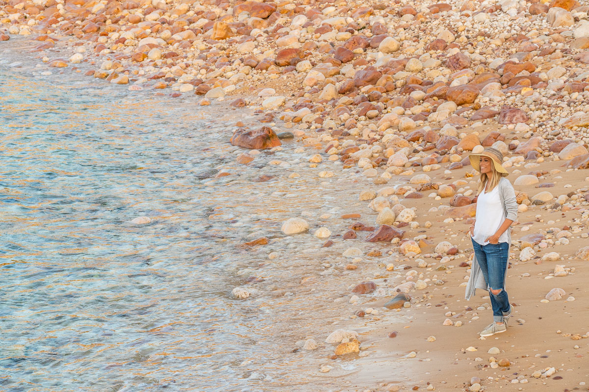 Frau steht am Strand mit vielen Steinen und denkt an den Urlaubsblues