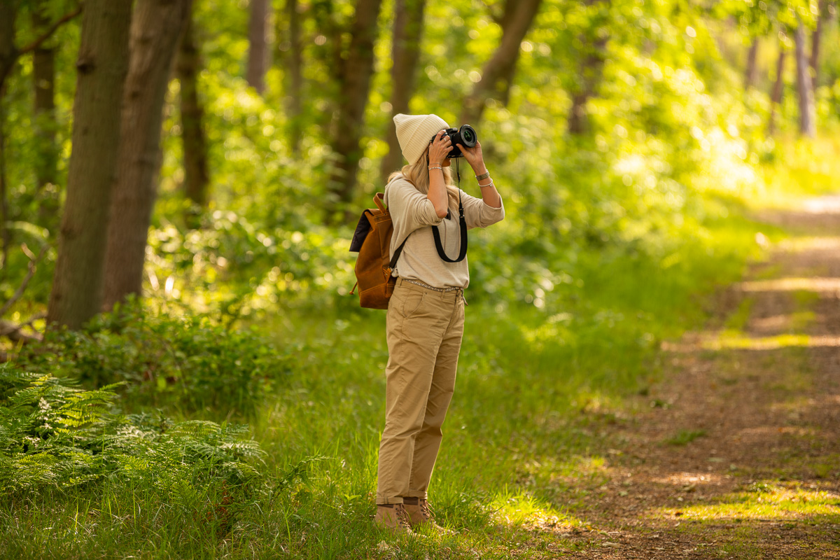 Frau steht im Wald und fotografiert Bäume auf Texel