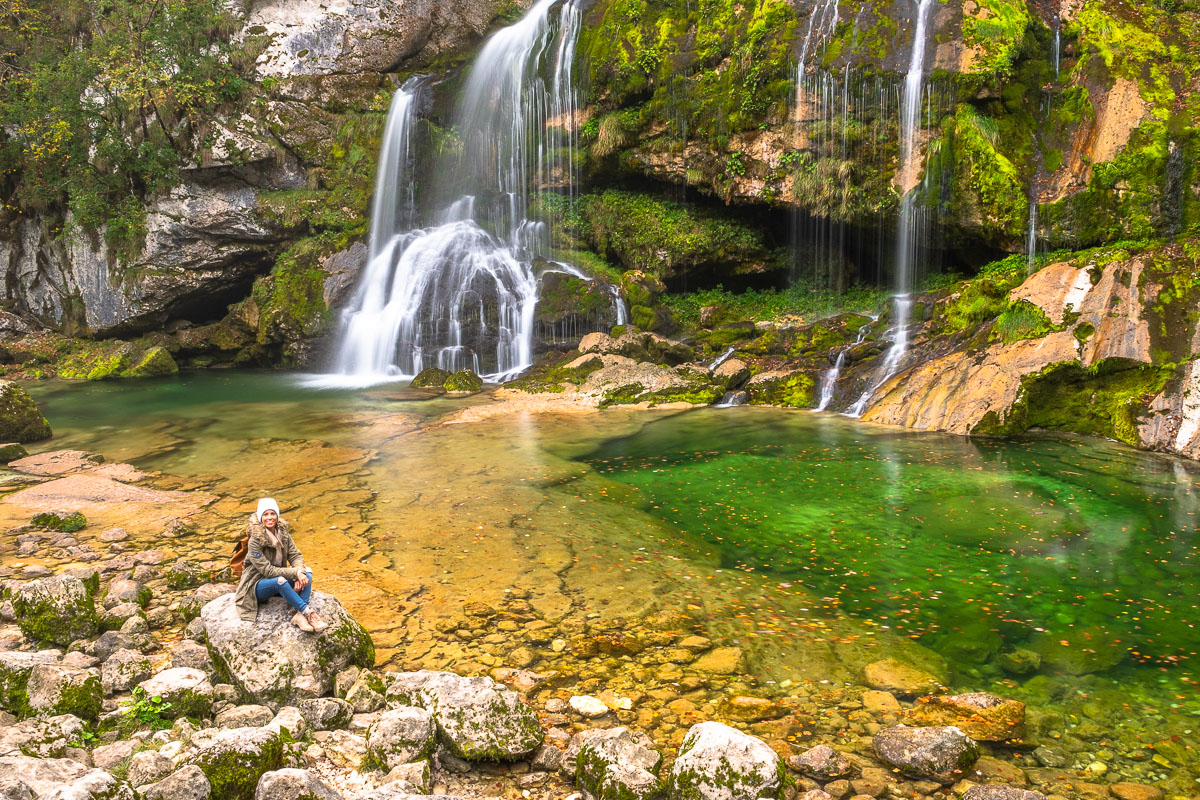 Frau sitzt vor einem Wasserfall im Soca Tal