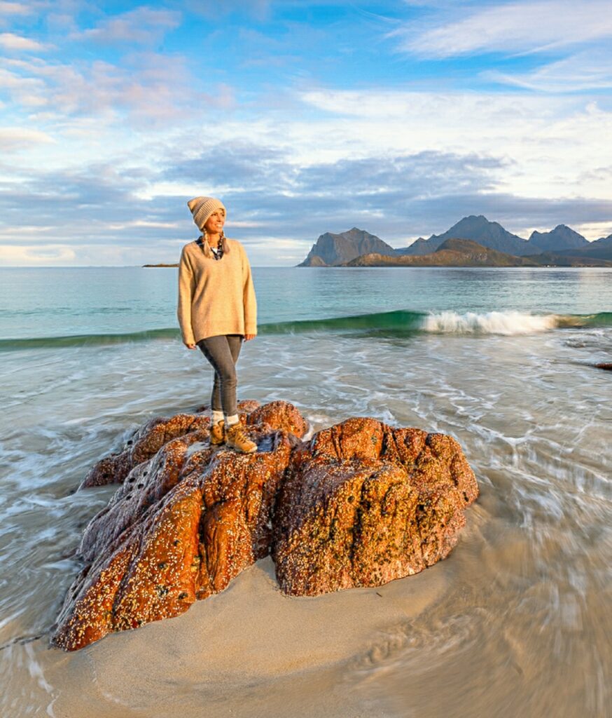 Frau steht auf einem Felsen und schaut auf das Meer